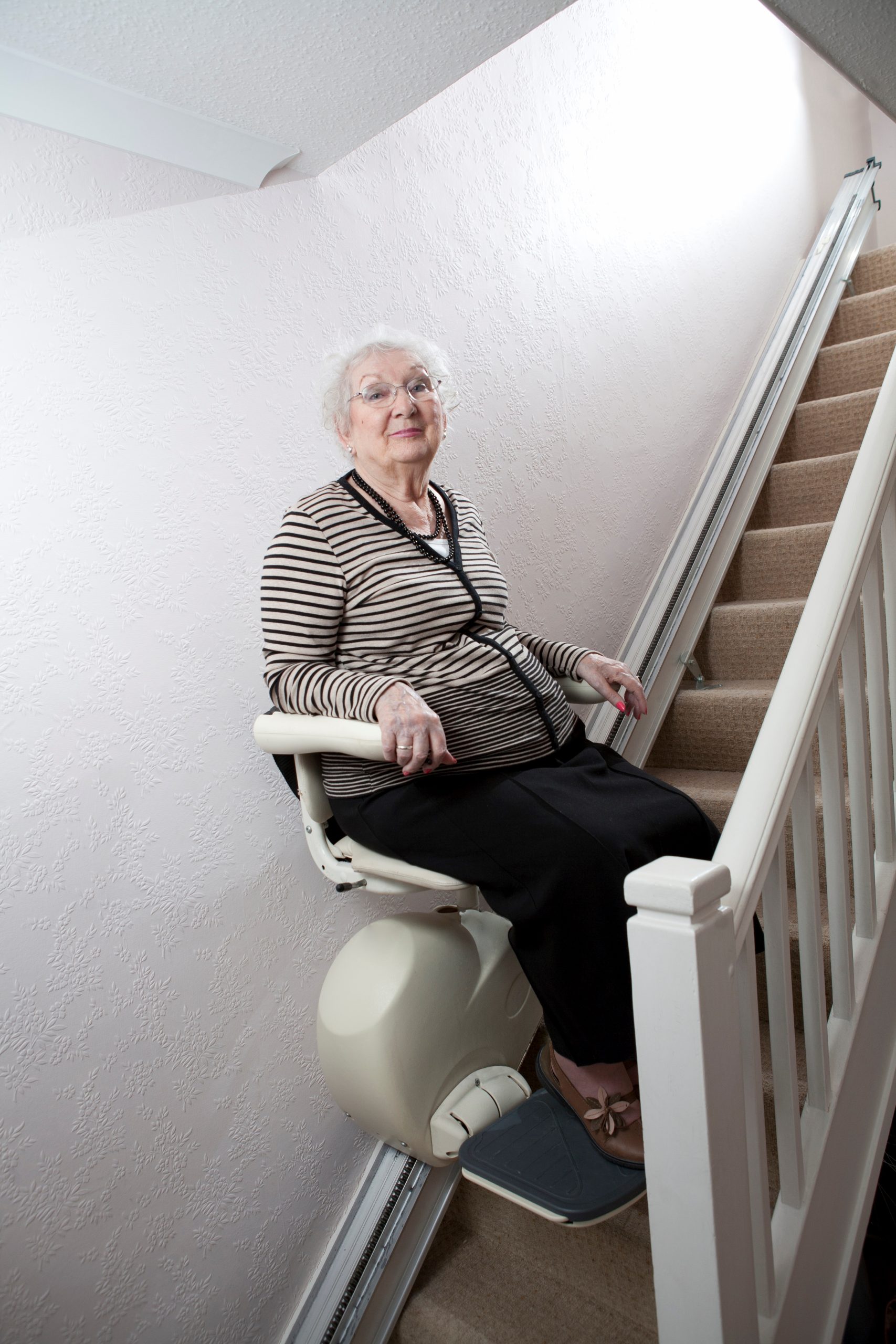 Eine ältere Frau sitzt auf einem Treppenlift in ihrem Zuhause